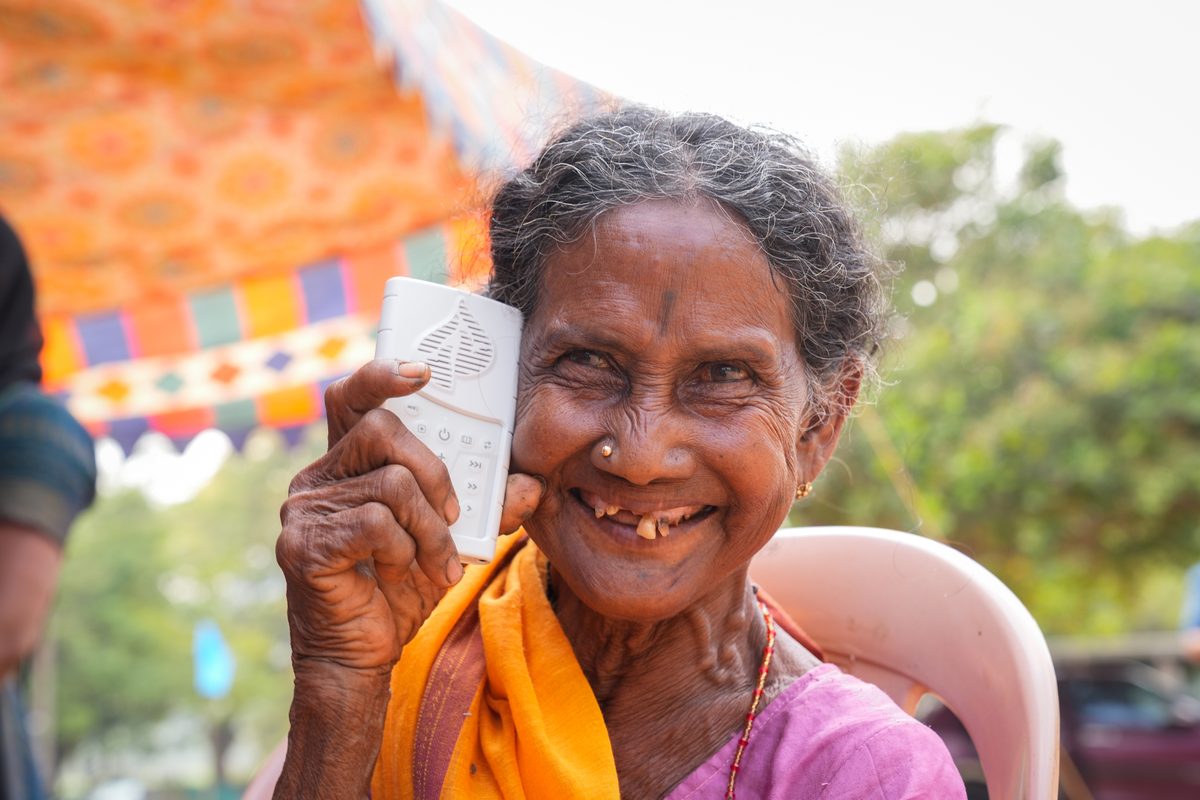 Elderly woman smiling while holding the WCOI Audio Bible device up to her ear